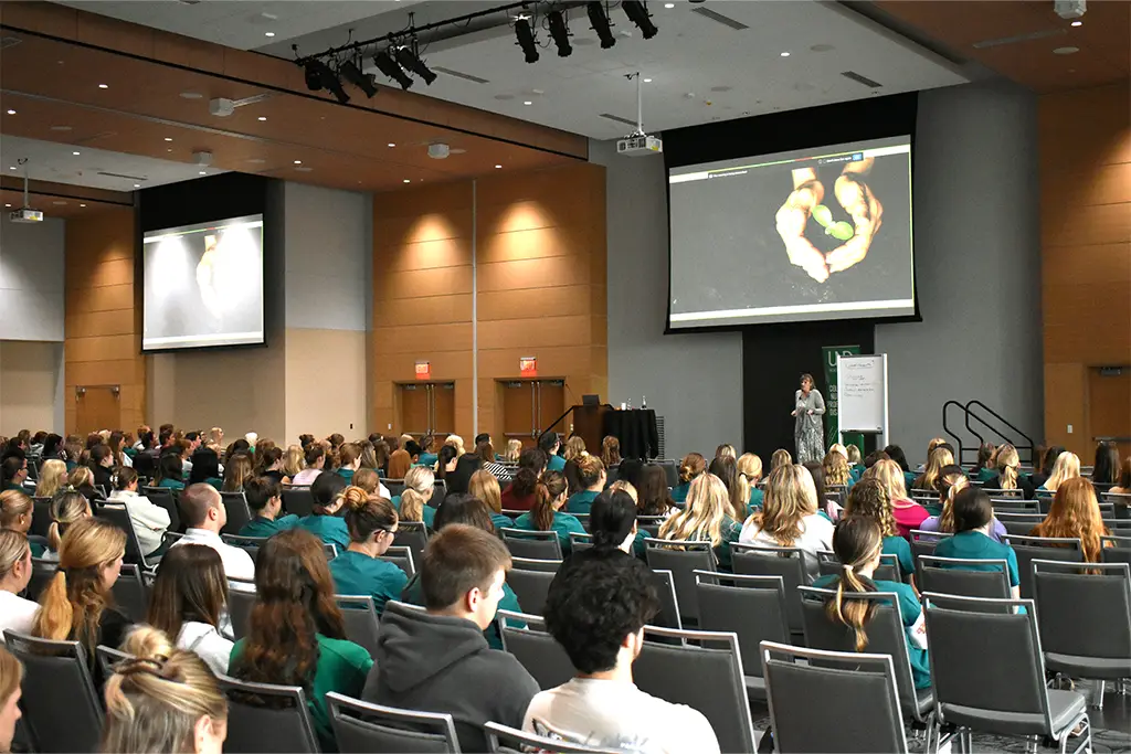 Susan Luparell speaks from the stage to an audience of CNPD students sitting in rows of chairs.