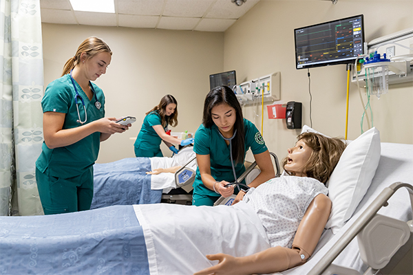 nursing students stand over a bed in the simulation center