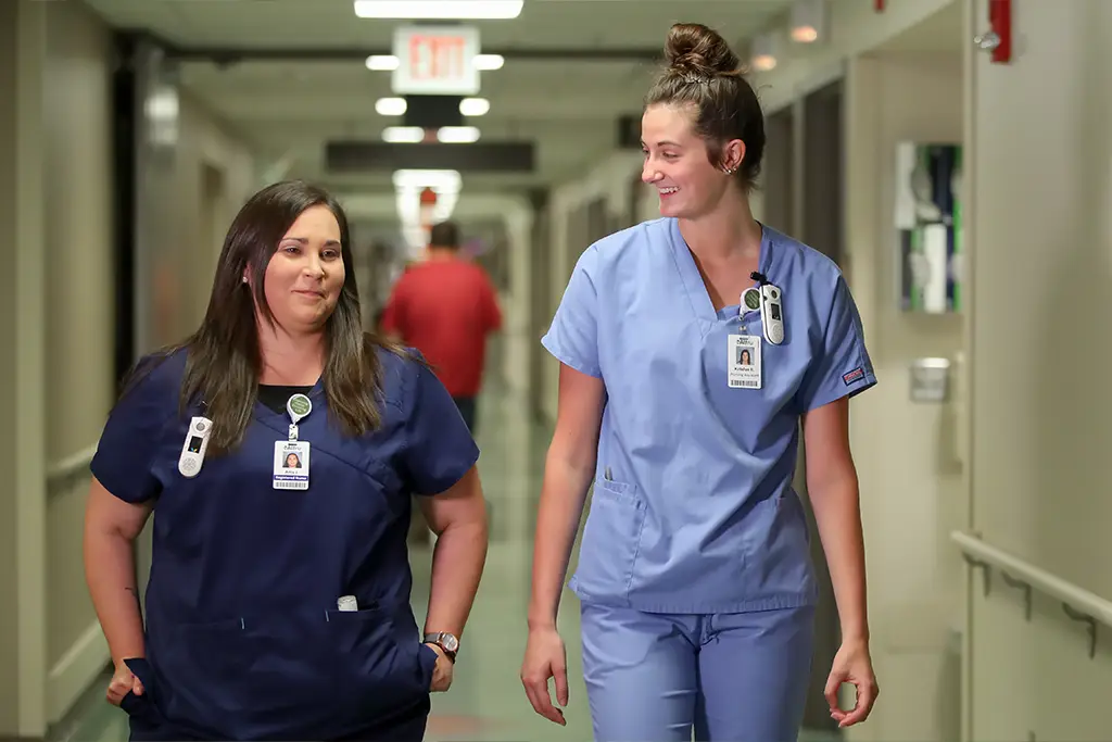 Two nurses in blue scrubs walk through the hallway of the clinic