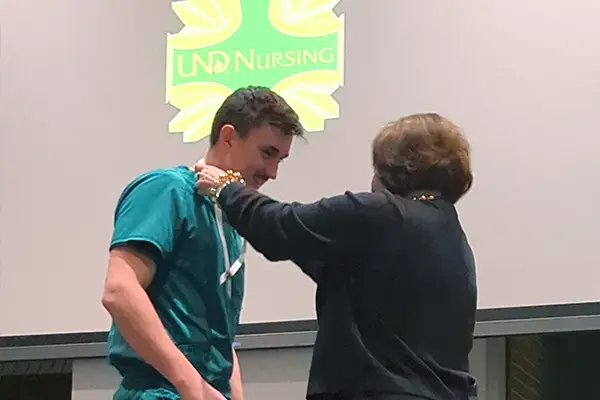 The UND Nursing Dean places a ribbon with a nursing pin on a RAIN graduate