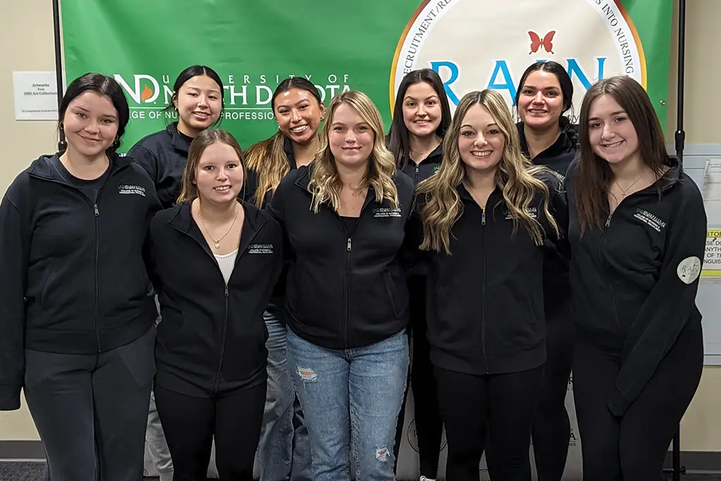 9 RAIN students gathered in front of a banner with the RAIN logo on green.
