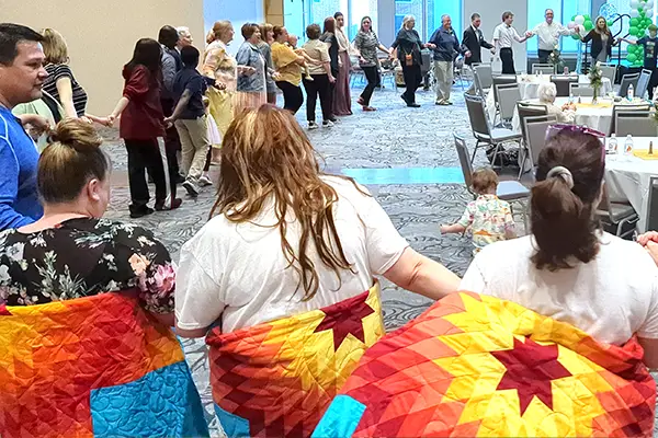 RAIN graduates hold hands and form a circle as they dance around the room. Bright star quilts hang off their shoulders