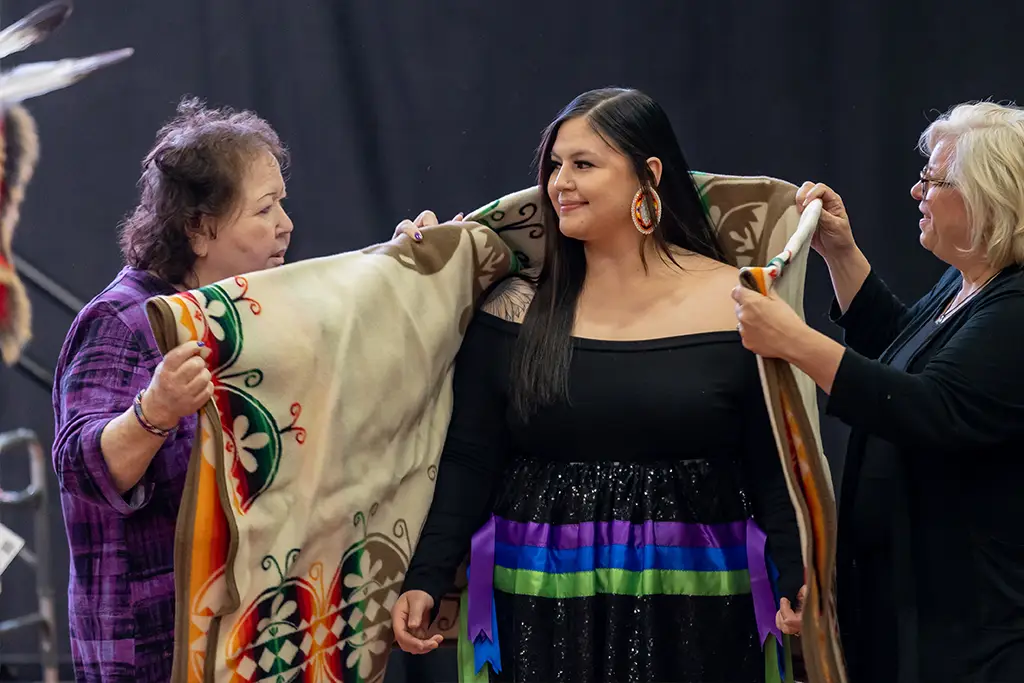 A RAIN graduate has a blanket placed on their shoulders by RAIN mentors and the department chair