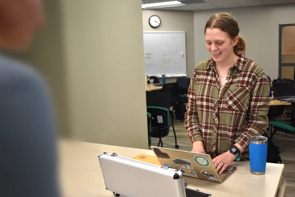 A student smiles while working on a laptop in a classroom setting